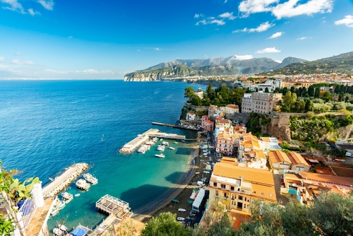 A scenic view of a colorful coastal town on a cliff with boats in the harbor.
