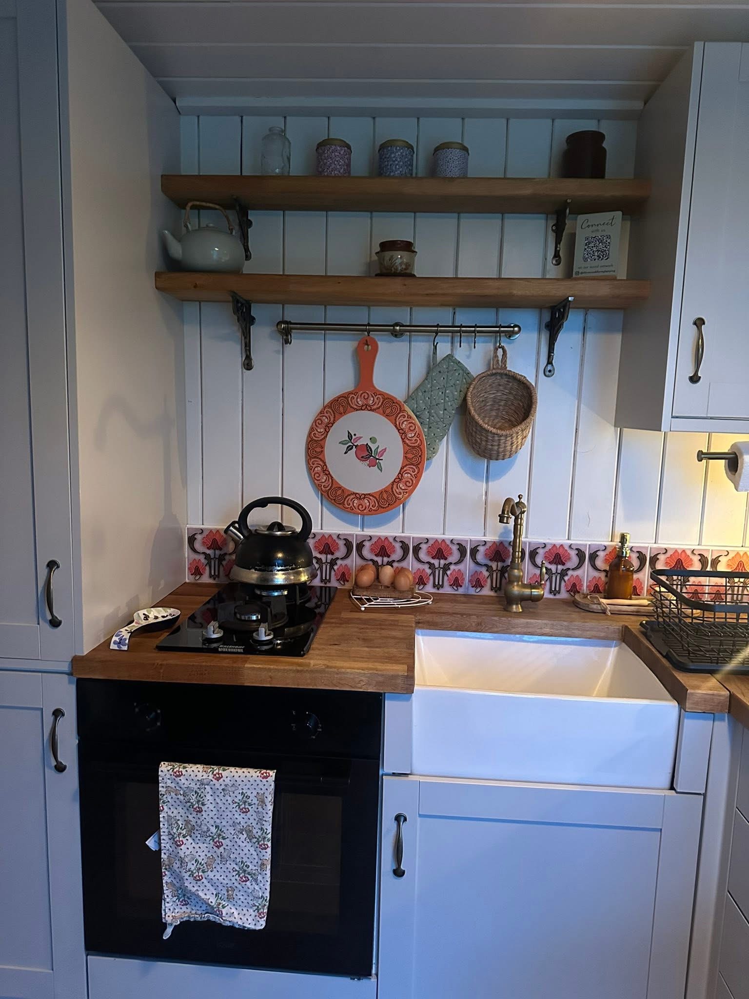 Cozy kitchen with stove, kettle, sink, and decorative shelves.