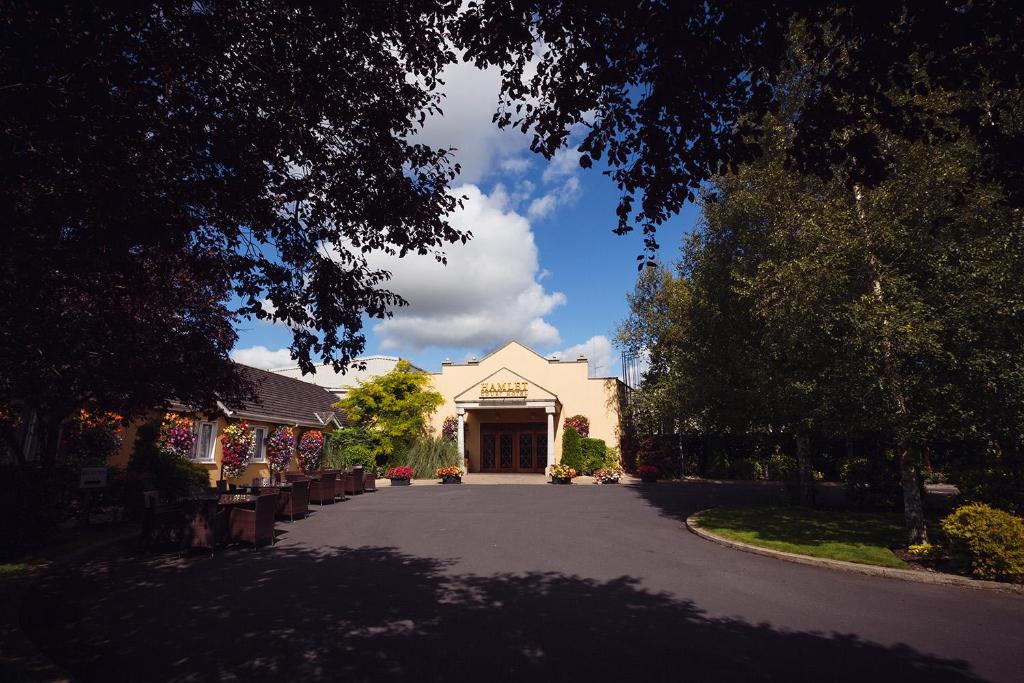 The entrance to the Hamlet Court Hotel, viewed from a tree-lined driveway on a sunny day.