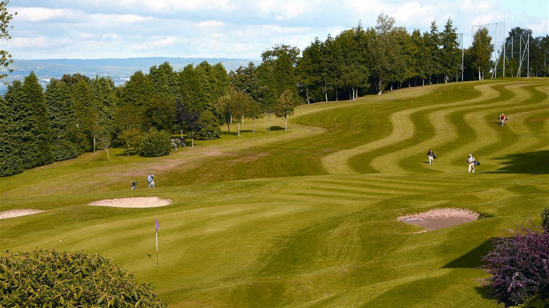 Golf course with players walking, surrounded by trees and sand bunkers.