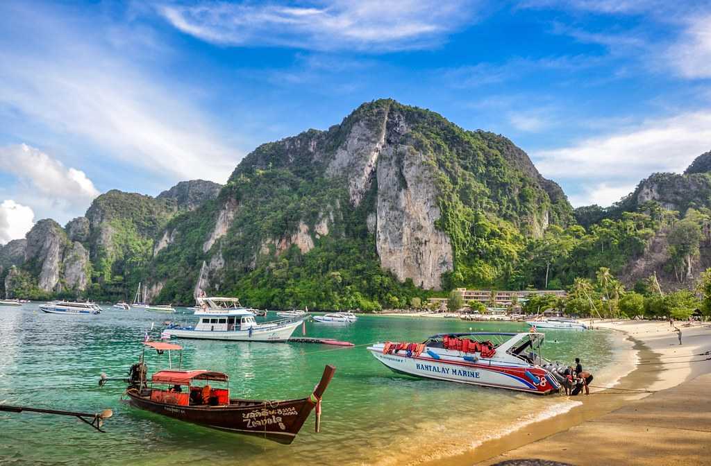 Boats on a tropical beach with lush green cliffs in the background.