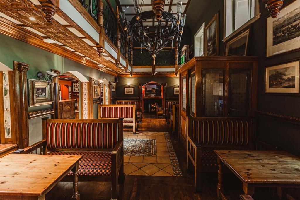 The ornate wooden interior of a traditional pub with high ceilings, booths, tables, and a large chandelier.