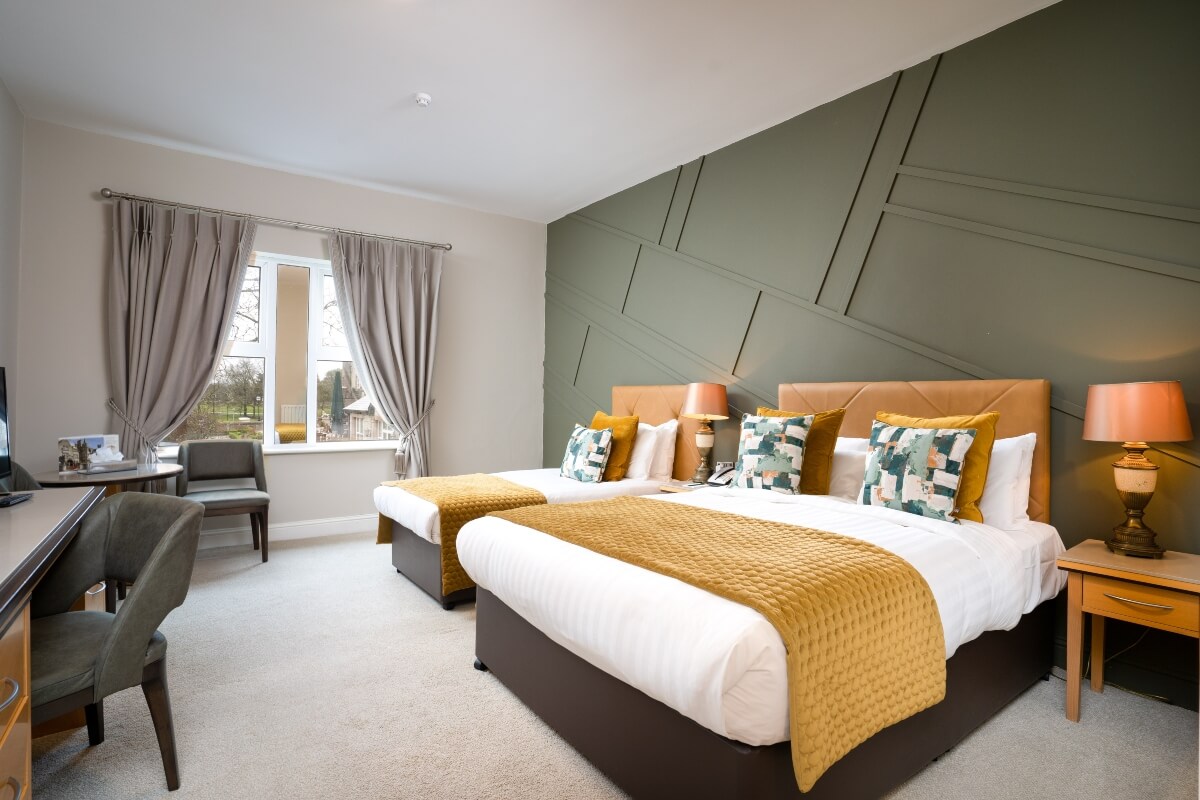 A hotel room with two beds, yellow throws, and a green geometric accent wall.