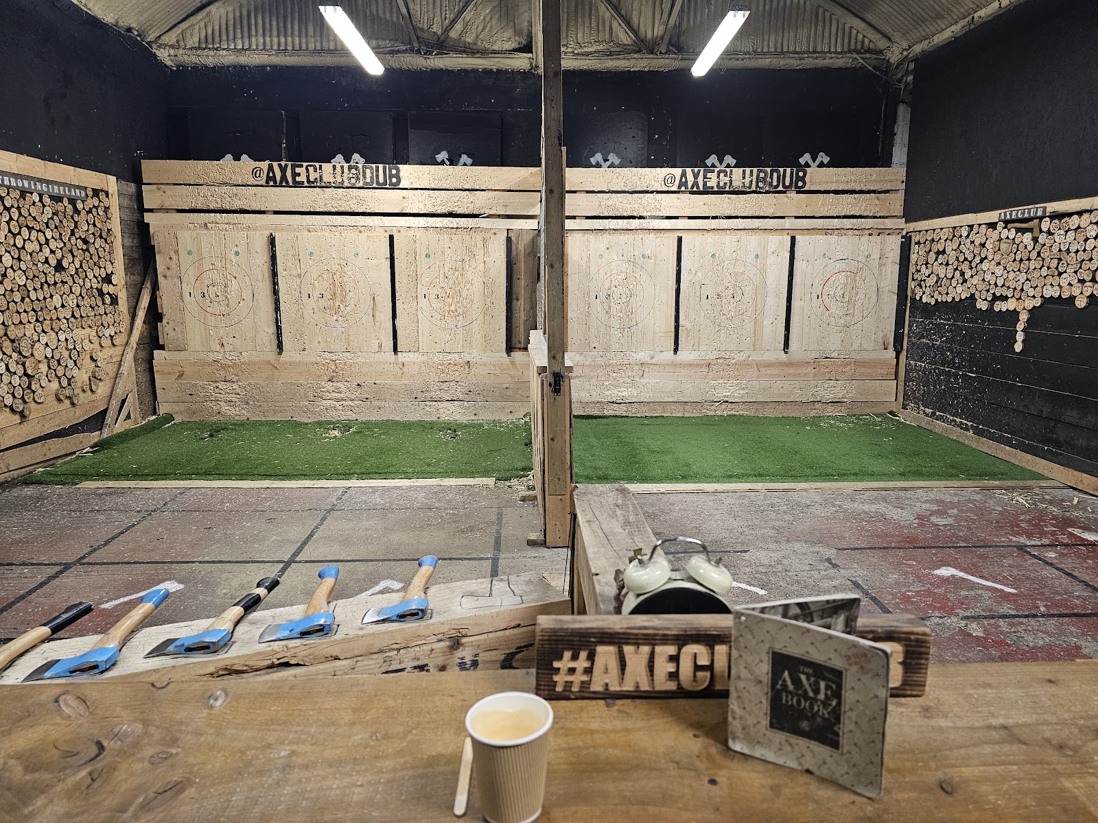An indoor axe-throwing venue with wooden targets and axes laid out on a table in the foreground.