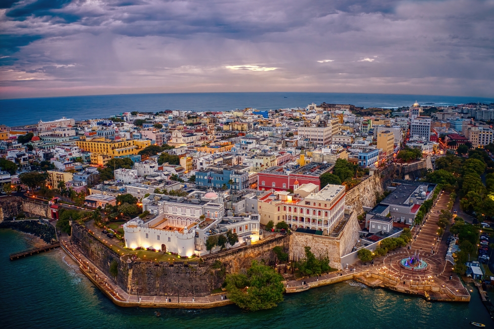 Aerial view of a colorful, historic coastal city with a stone fort at dusk.