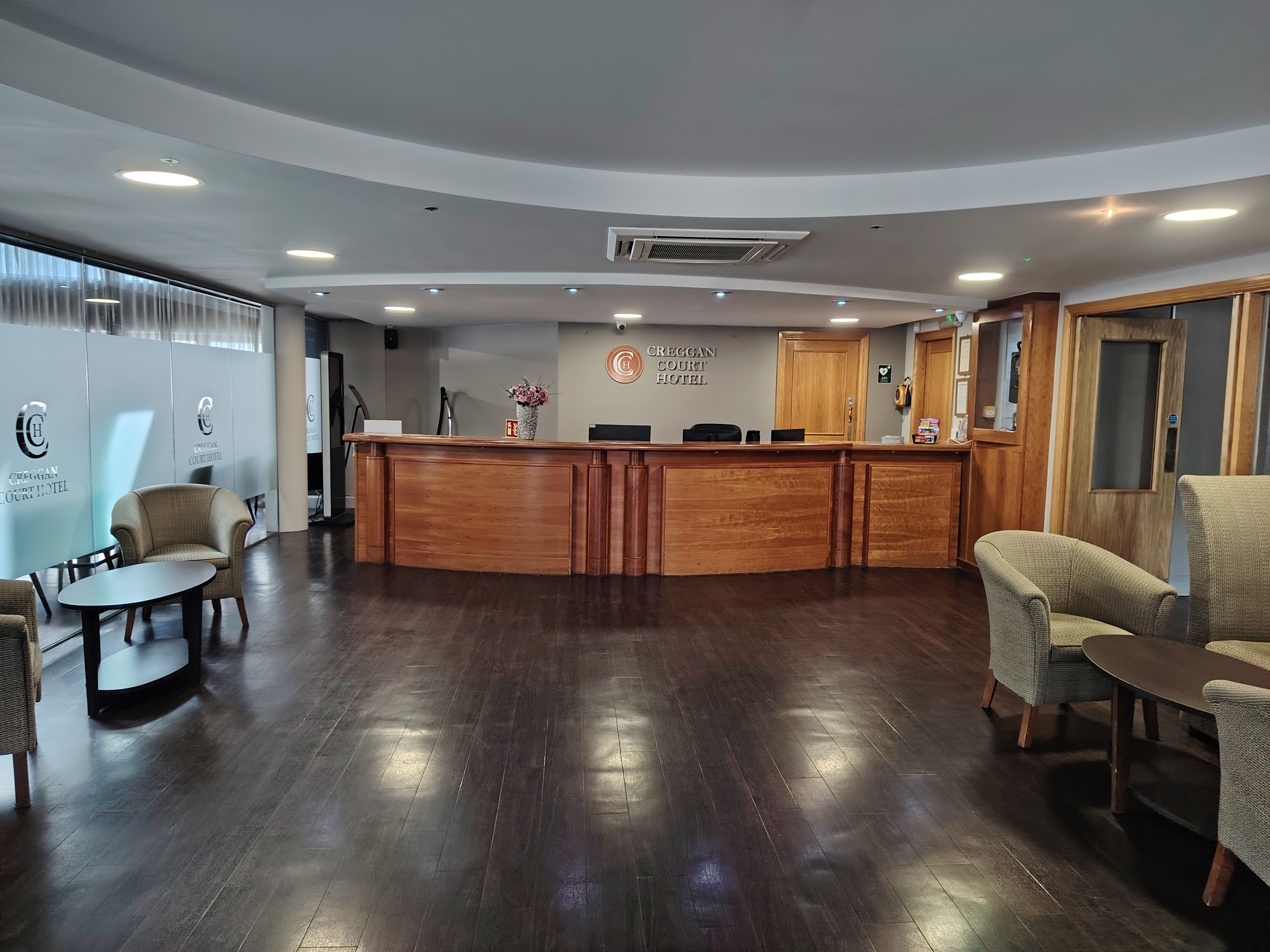 The spacious lobby and reception desk of the Creggan Court Hotel with dark wood floors and seating areas.