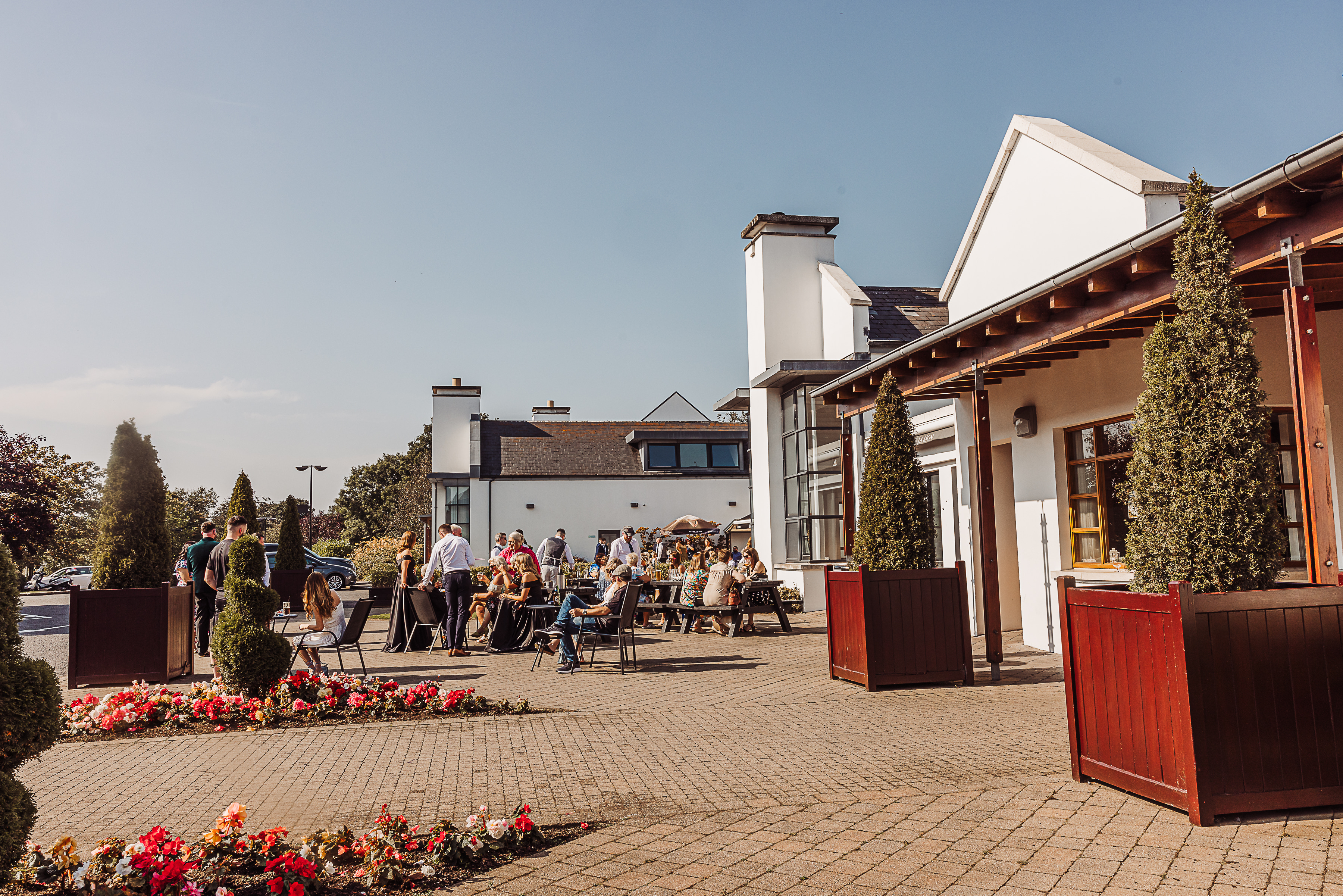A group of people socializing on a sunny day at tables on a large paved hotel patio.