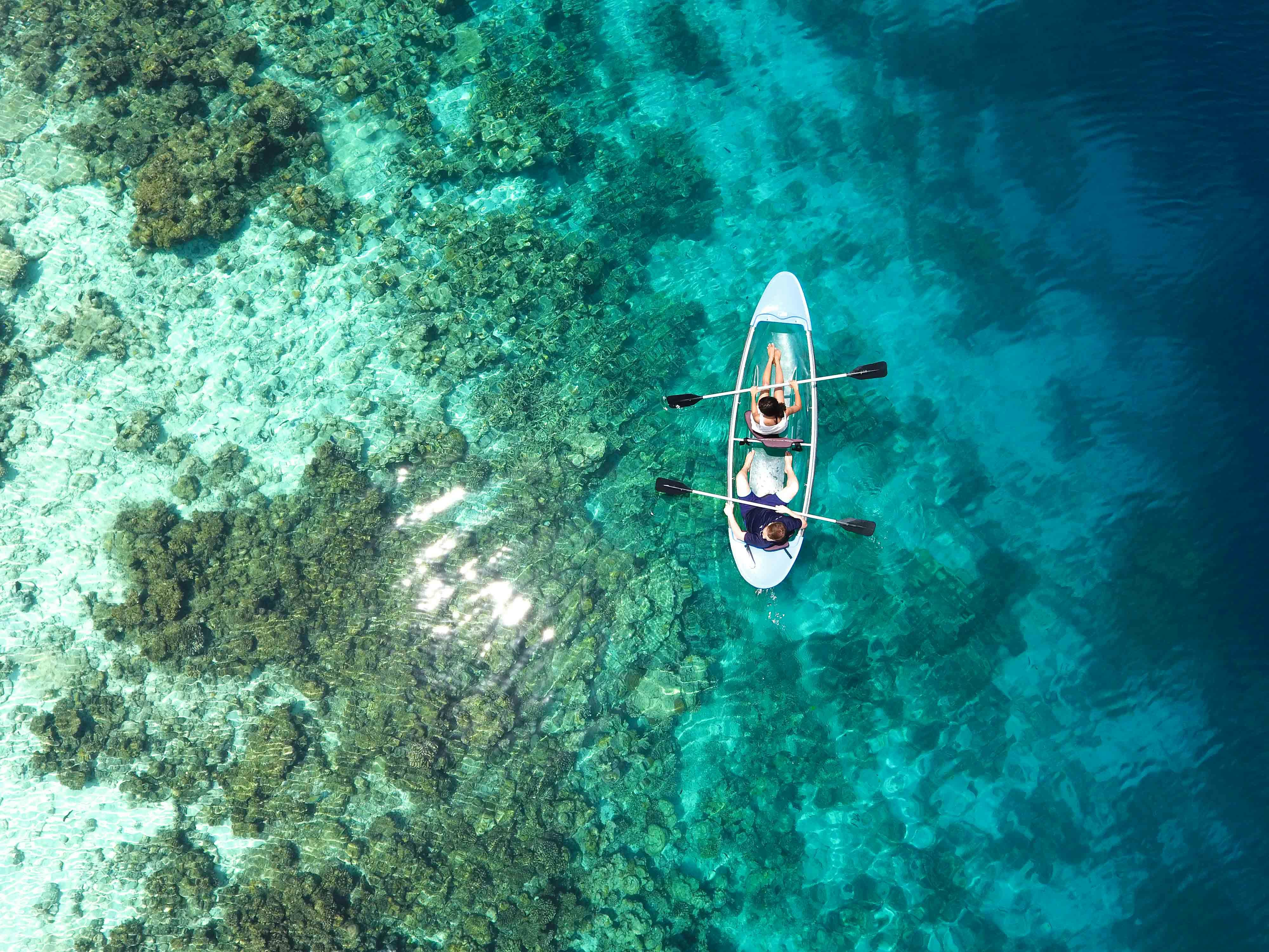 Two people kayaking over clear turquoise water with visible coral below.