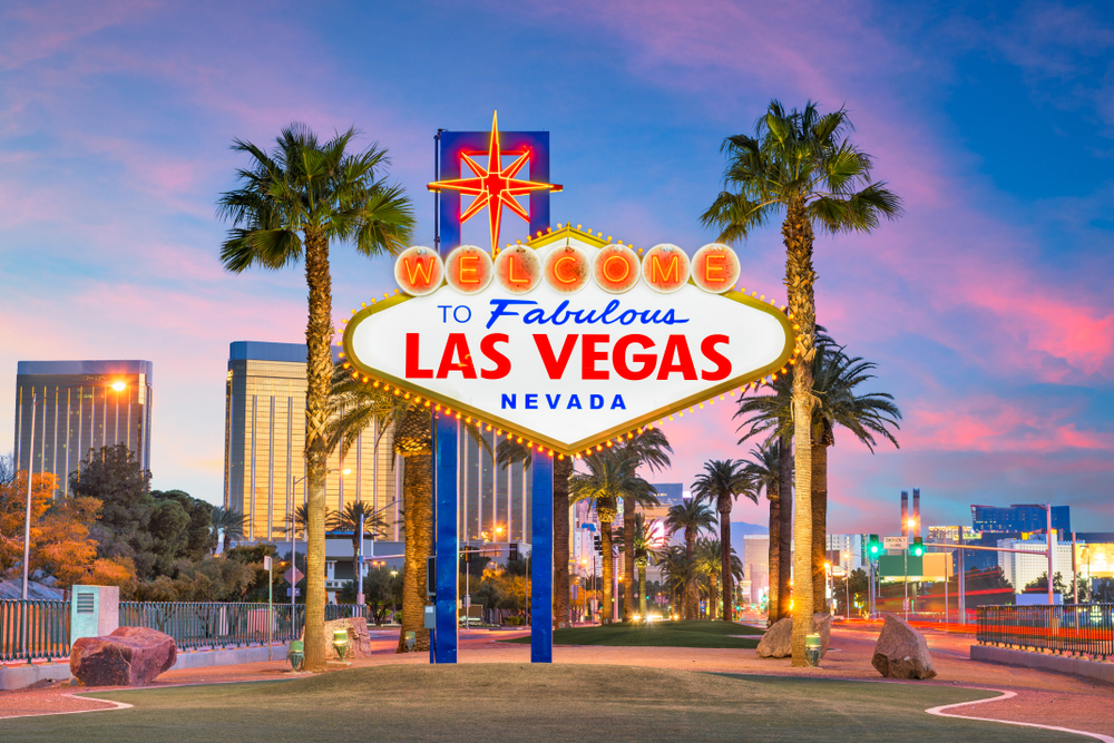 The 'Welcome to Fabulous Las Vegas' sign illuminated at dusk, surrounded by palm trees and city buildings.