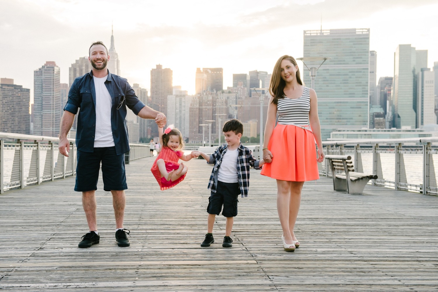 Family of four walking on a boardwalk with city skyline in background.