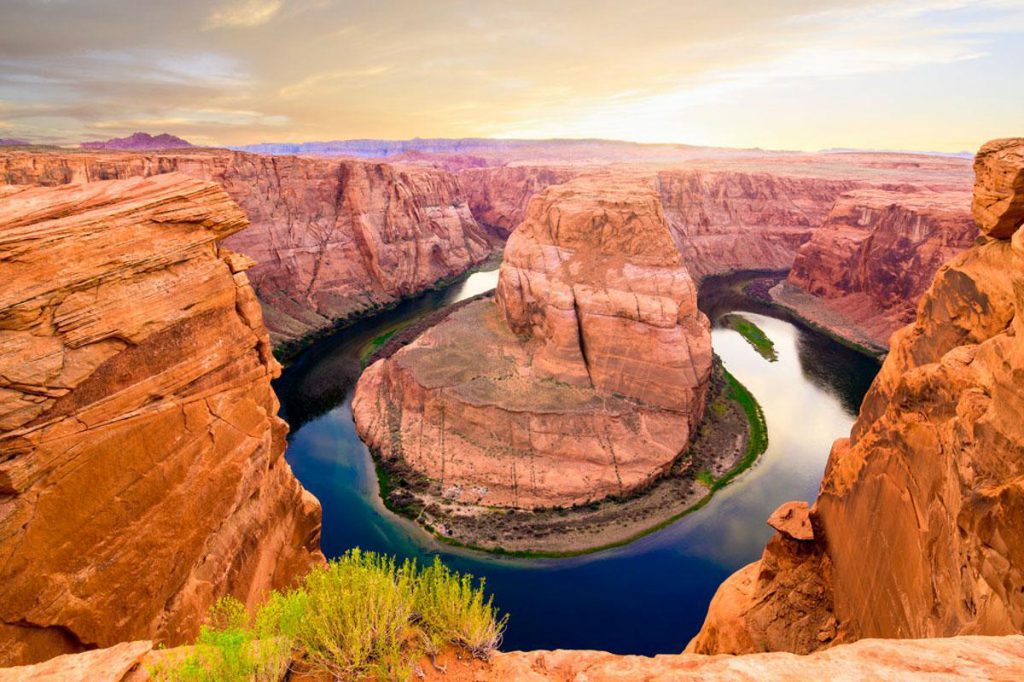 Aerial view of a river bending around a large rock formation at sunset.