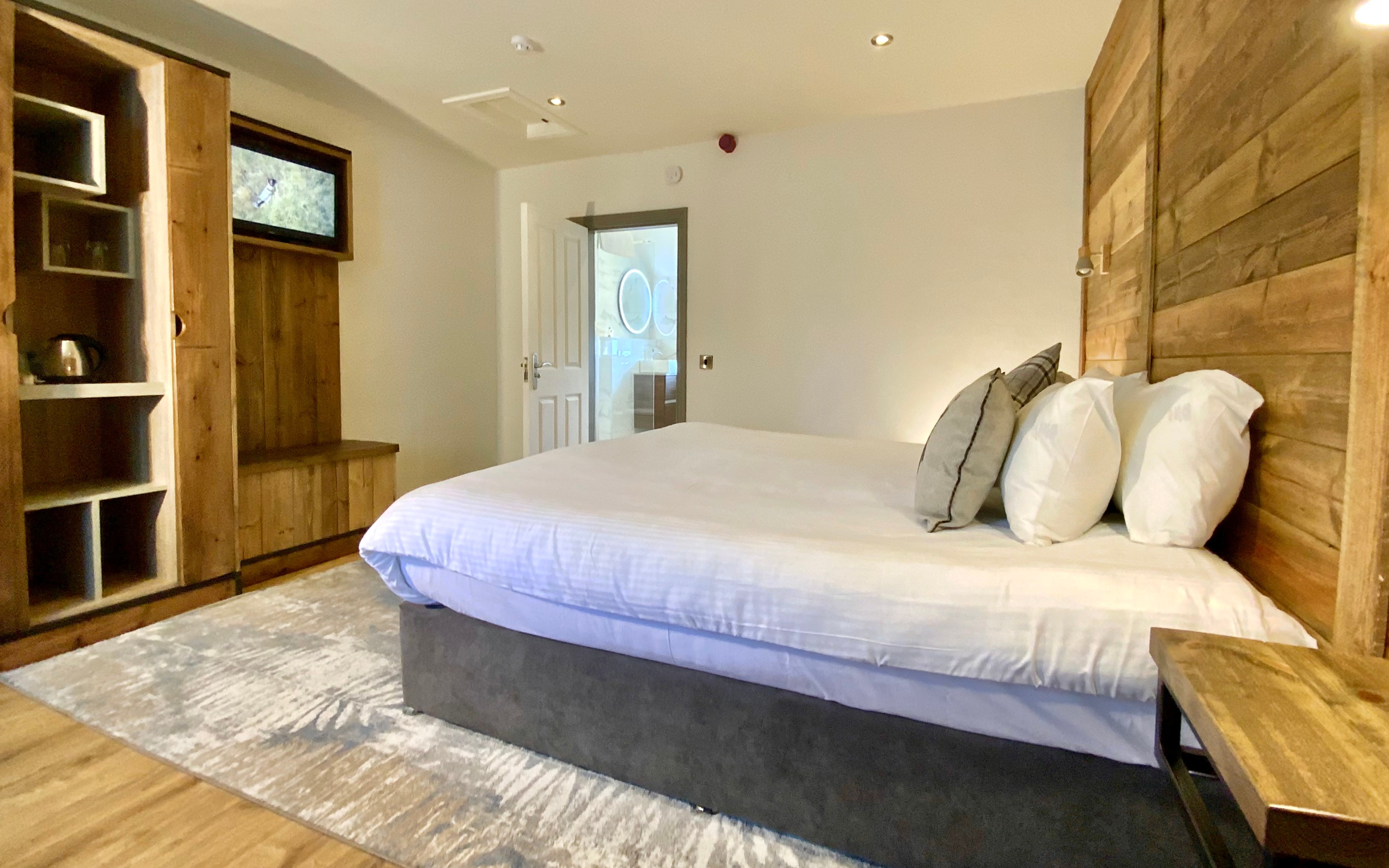 A hotel bedroom with a large bed, rustic wooden furniture, and a doorway leading to a modern bathroom.