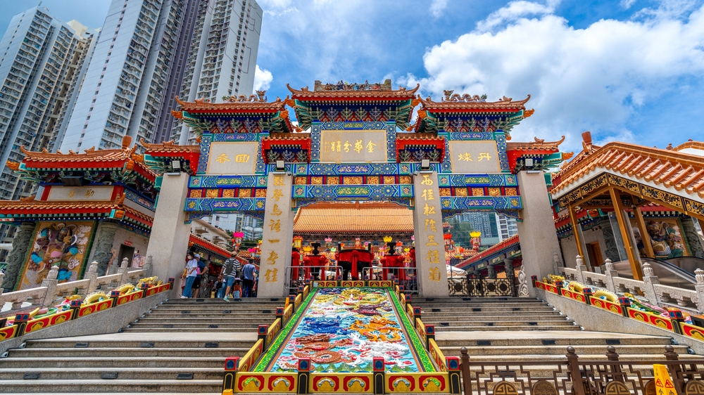 An ornate, colorful Chinese temple entrance with a grand staircase, set against a modern high-rise building.