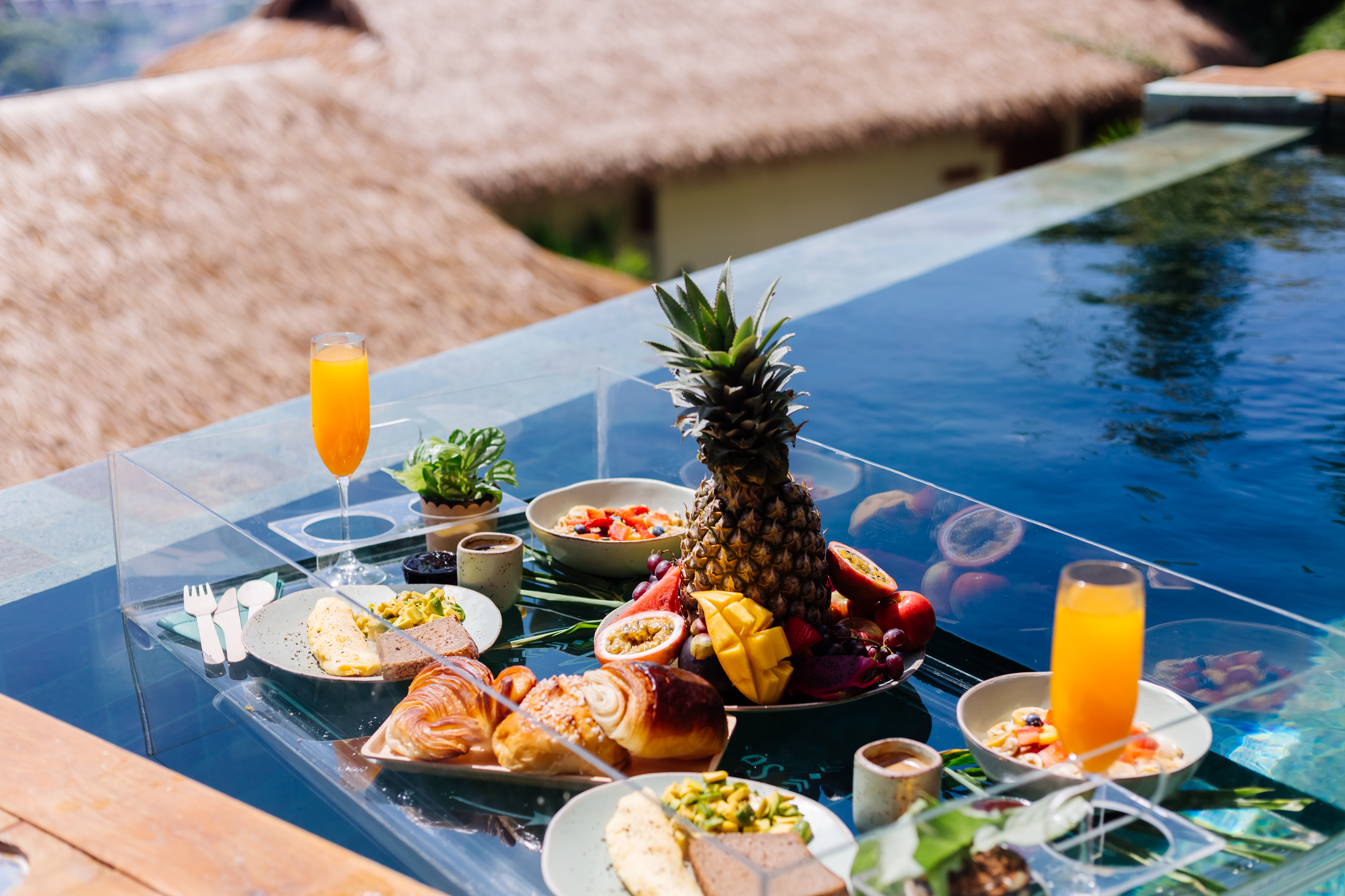Breakfast spread with fruit, pastries, and drinks by a poolside.