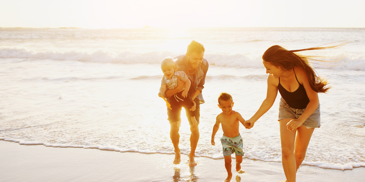 Family playing on the beach at sunset, with waves in the background.