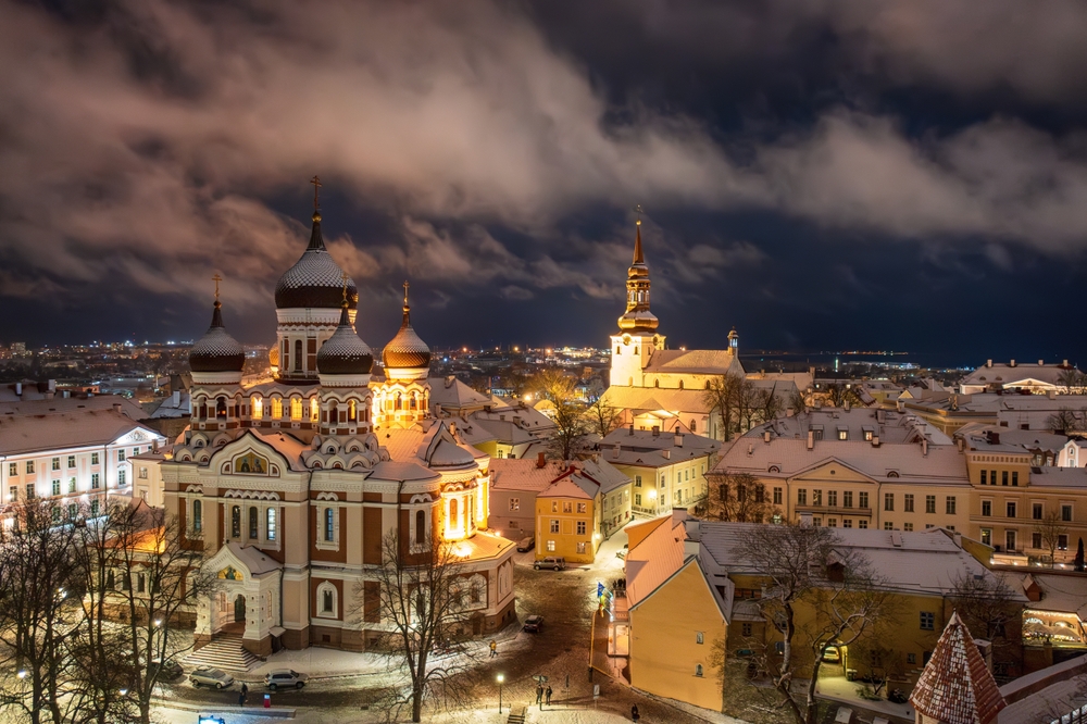 A snowy cityscape at night, with an illuminated cathedral featuring onion domes in the foreground.