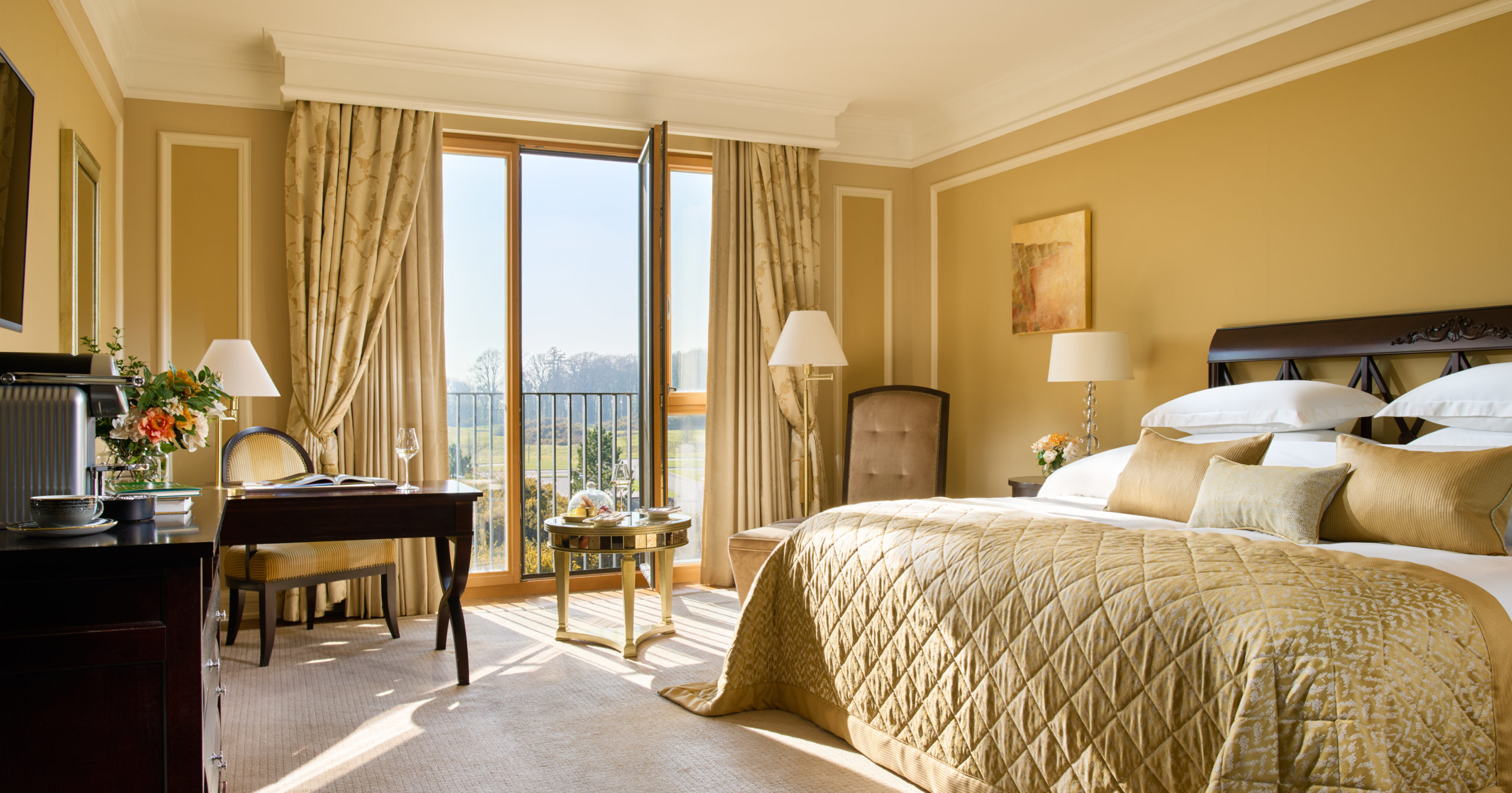 Elegant hotel room with a large bed, desk, and open balcony doors.