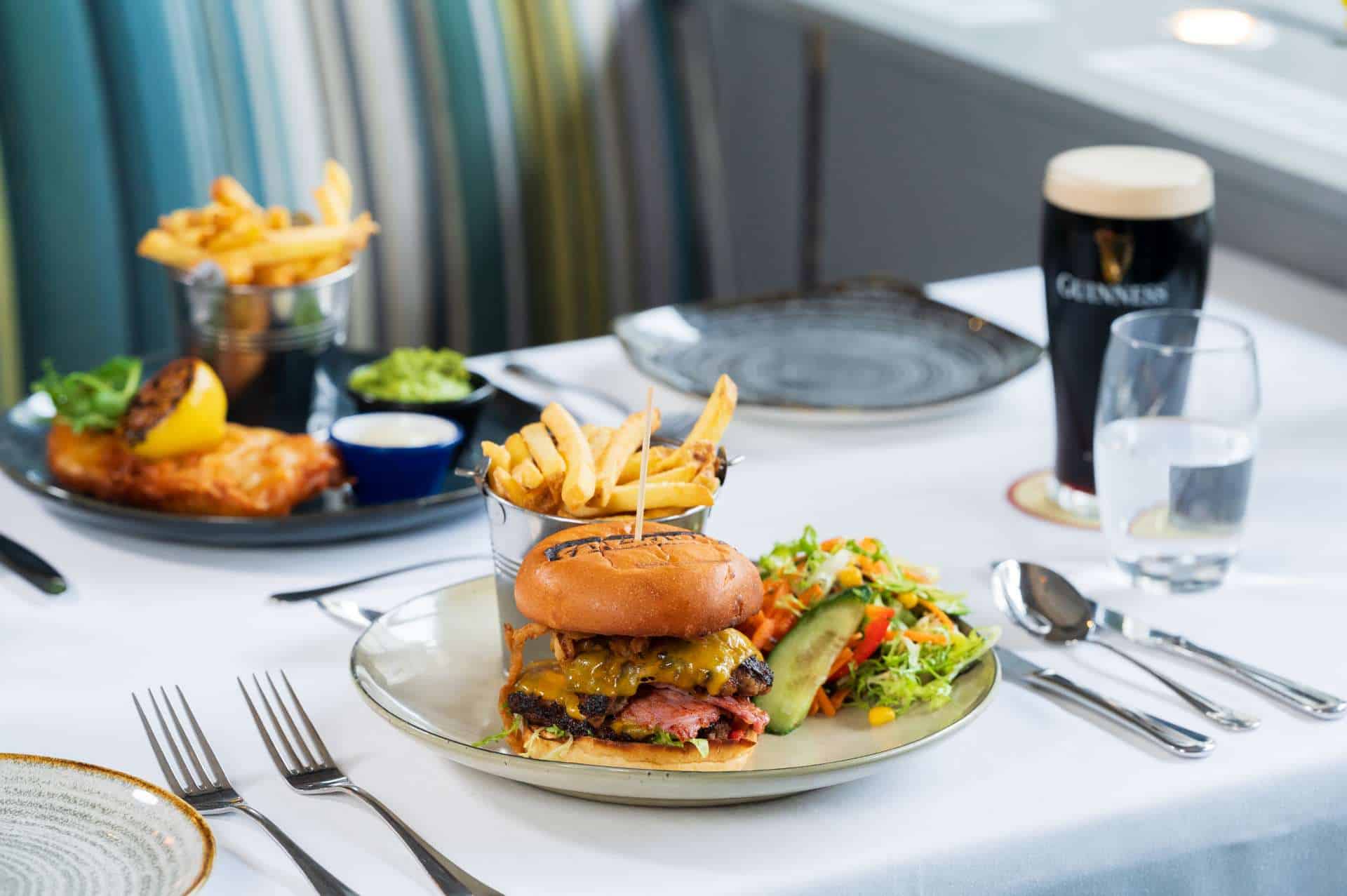A table set with plates of a burger and fries, fish and chips, and a pint of Guinness.