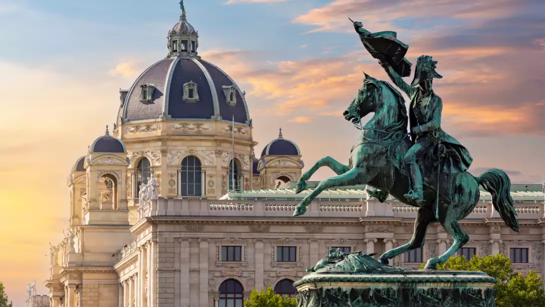 An equestrian statue of a man on a horse in front of a large domed building at sunset.