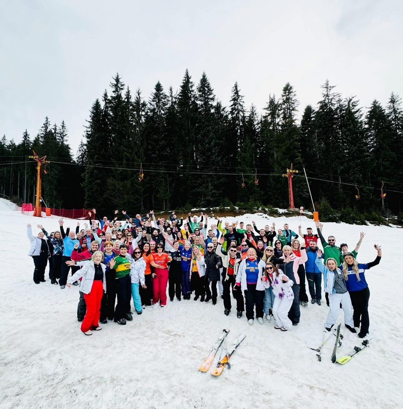 Large group of people posing on a snowy slope with trees in the background.