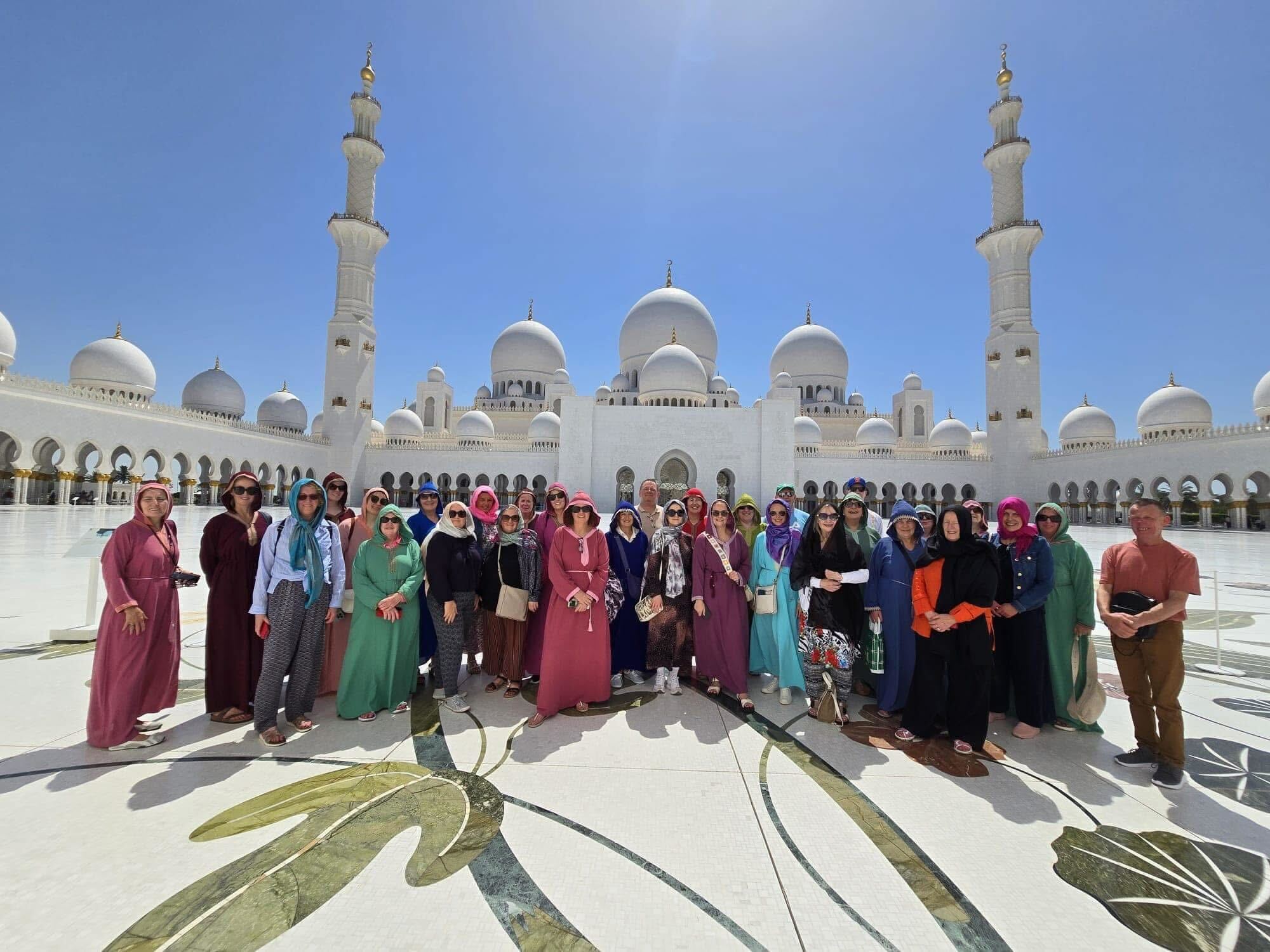 Group of people posing in front of a large white mosque with domes and minarets.