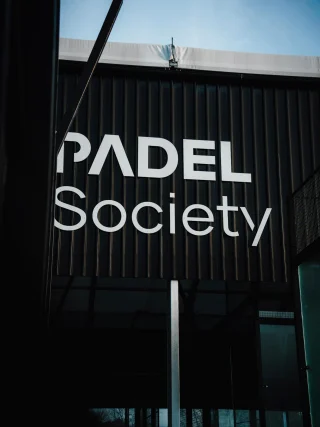 The white 'Padel Society' sign on the dark, vertically-paneled exterior of a building.