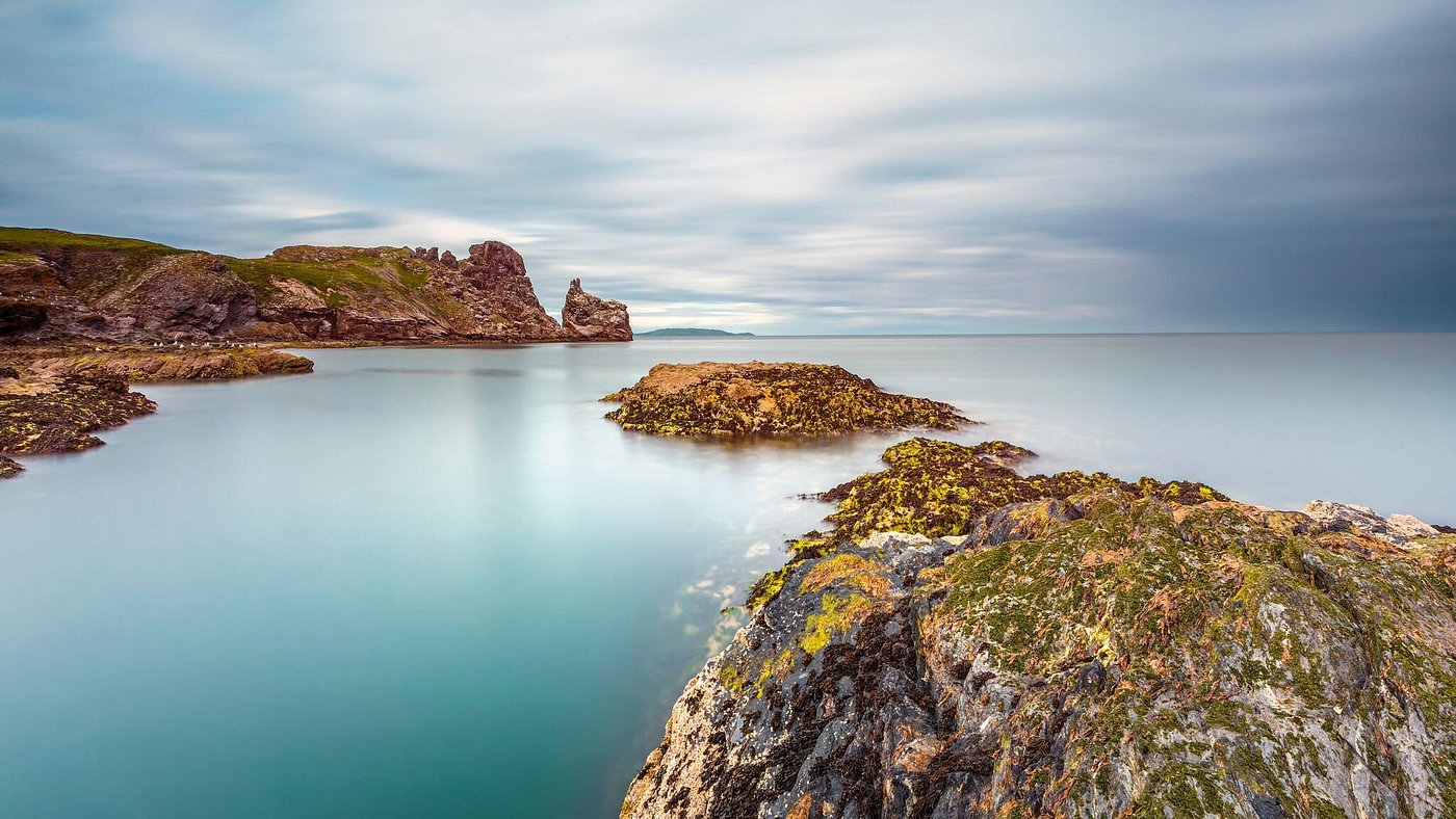 Rocky coastline with calm sea and cloudy sky.