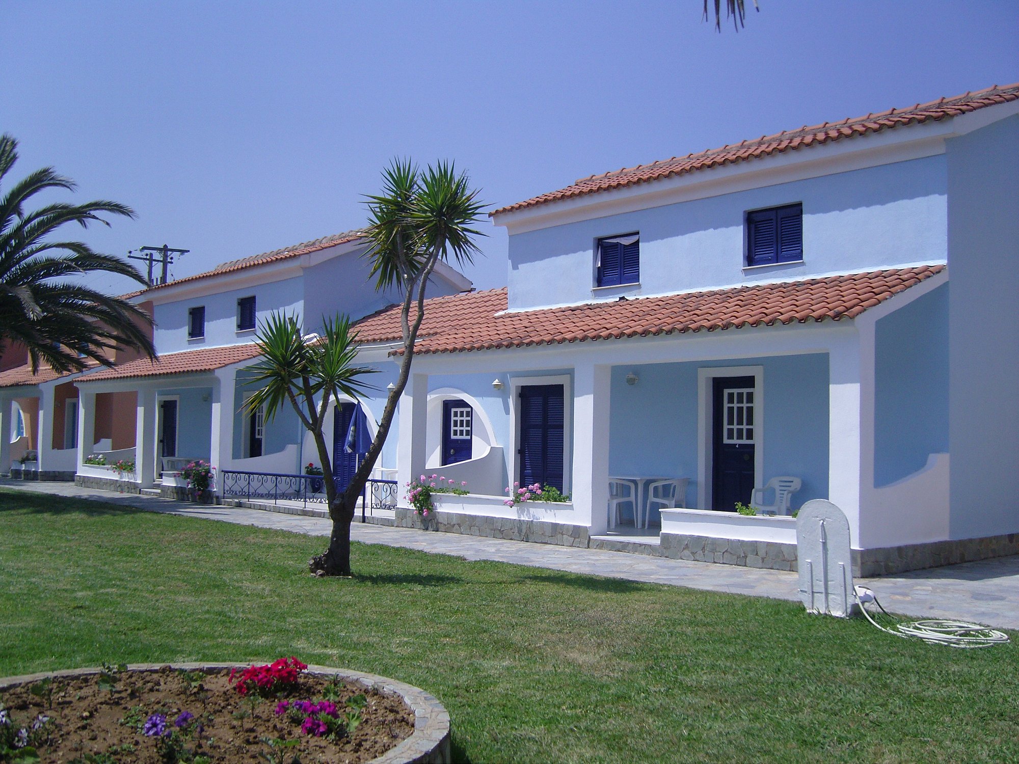 Row of blue and white houses with red roofs and palm trees.