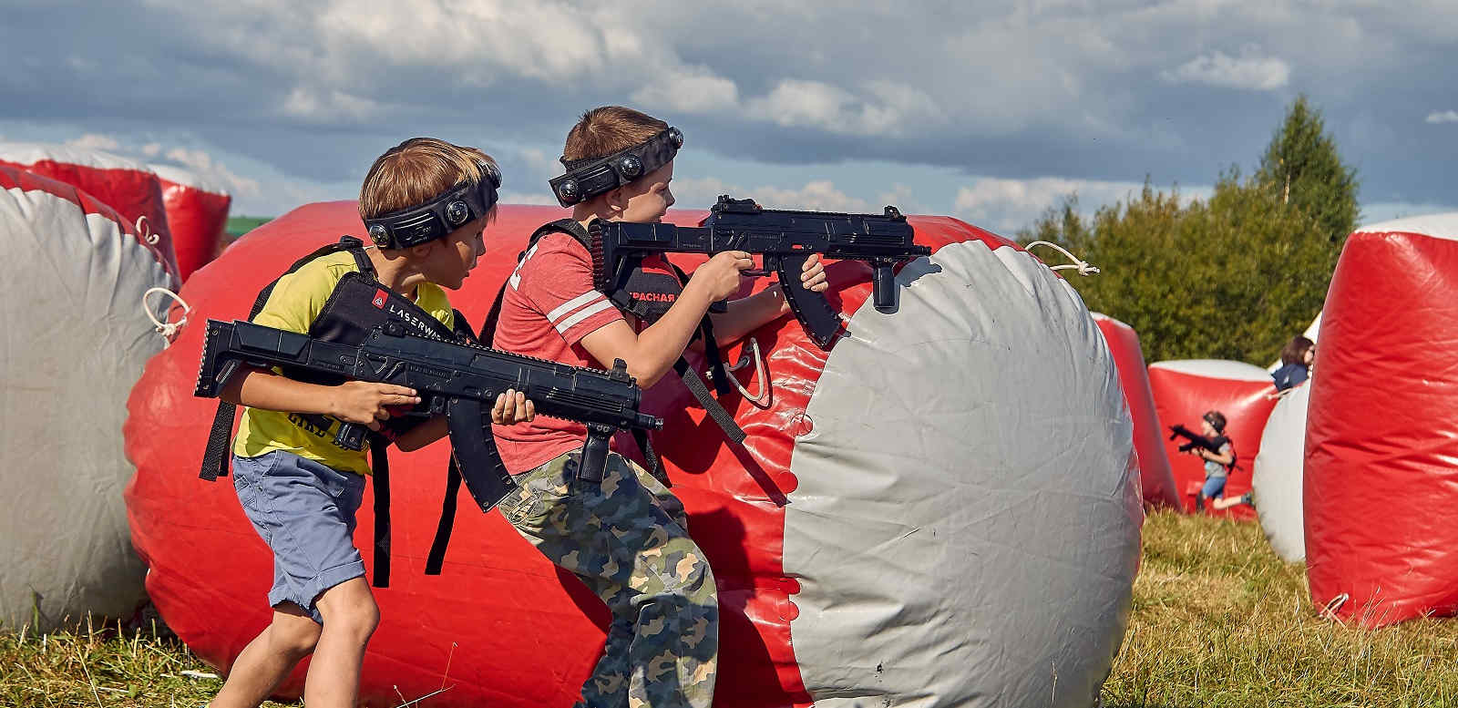 Children playing laser tag behind inflatable barriers outdoors.
