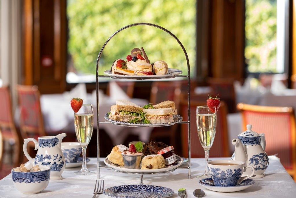 A three-tiered stand with sandwiches, cakes, and scones, served with champagne and tea on a dining table.
