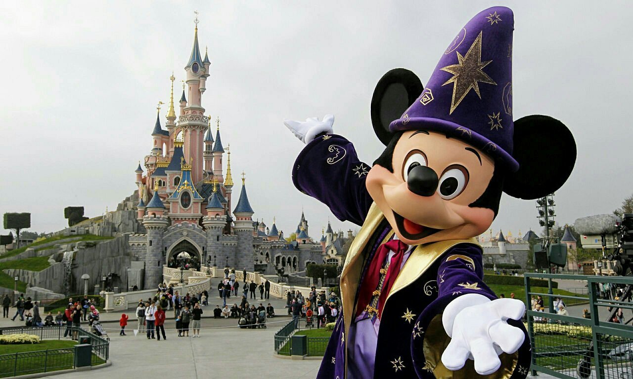 Character in wizard costume in front of a castle with people around.