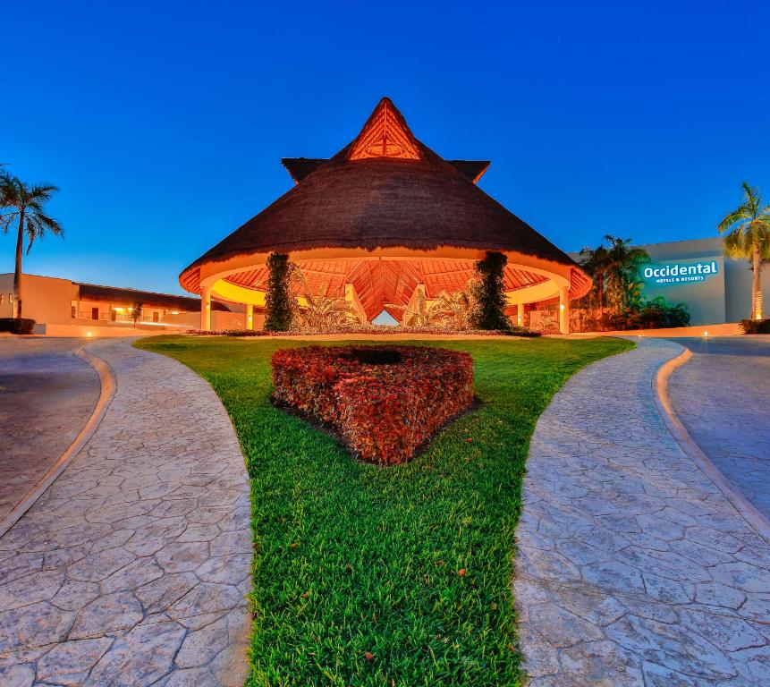 Thatched-roof building with landscaped entrance and palm trees at dusk.
