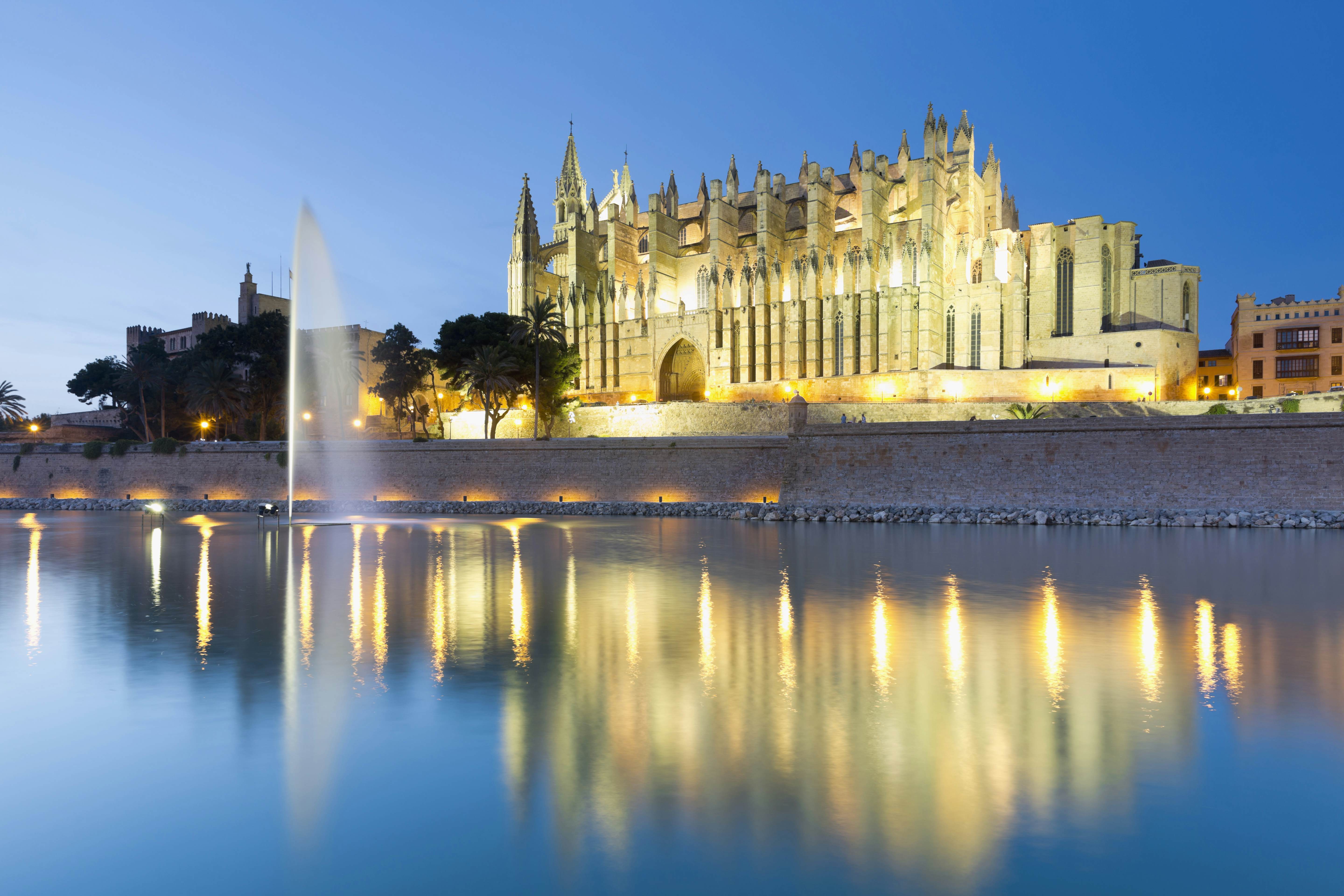 Illuminated cathedral with reflection in water at dusk.