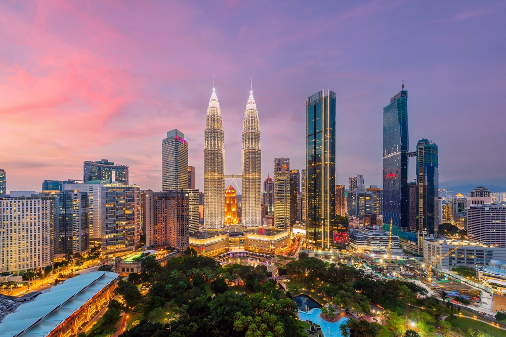 A city skyline with illuminated twin towers and other skyscrapers against a colorful sky at dusk.