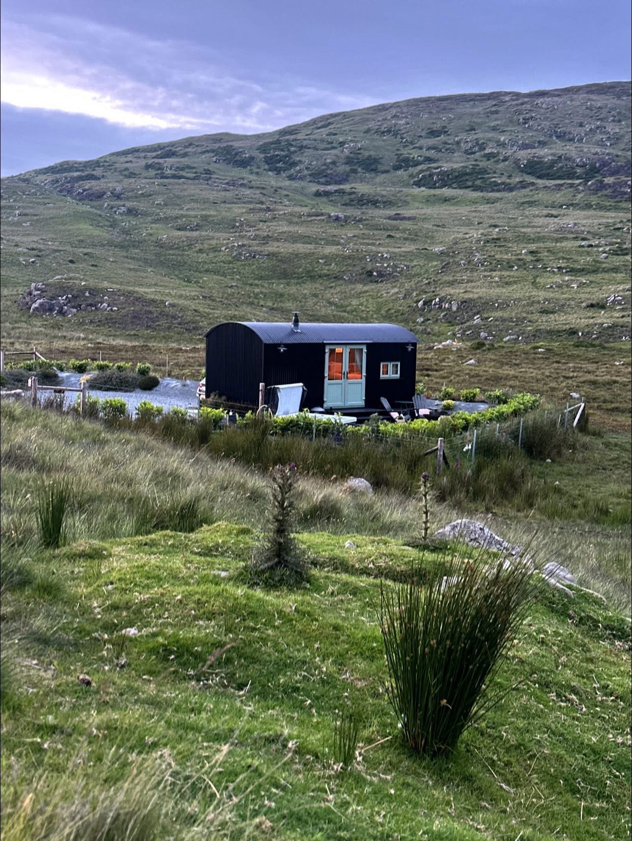 Small black cabin in a grassy, hilly landscape.