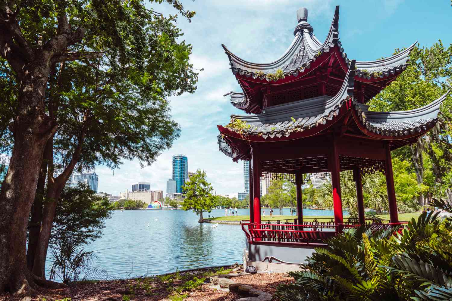 Traditional pavilion by a lake with city skyline in the background.