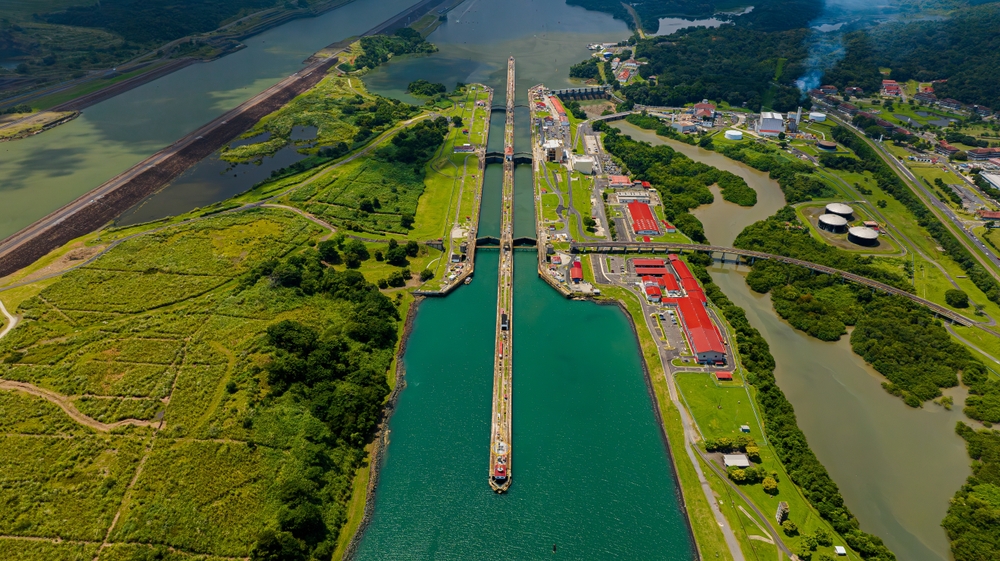 An aerial view of a large ship passing through a canal with locks, surrounded by lush green terrain.