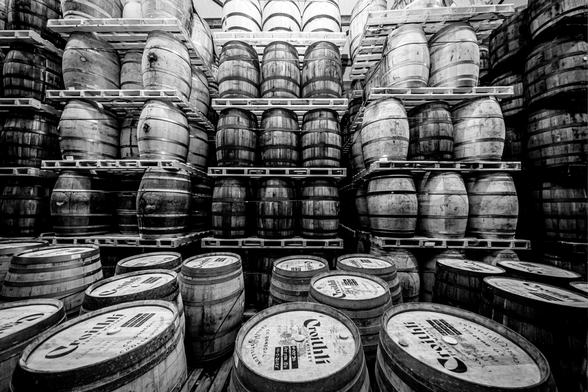 Black and white image of stacked wooden barrels in a warehouse.