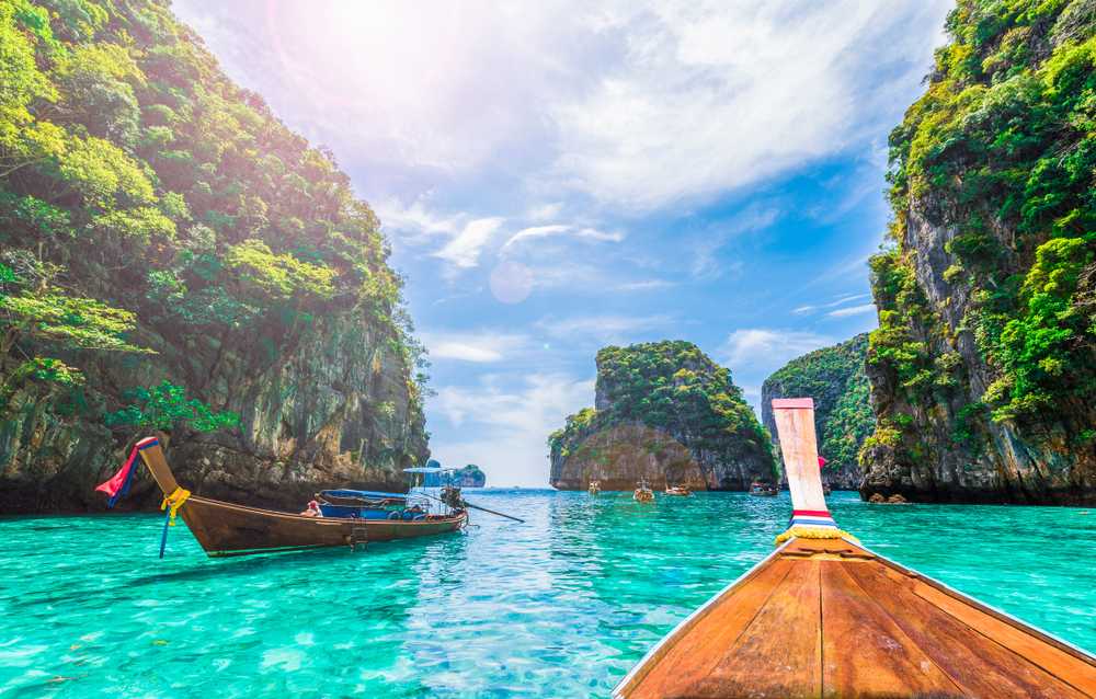 Wooden boats on turquoise water between lush green cliffs under a bright sky.