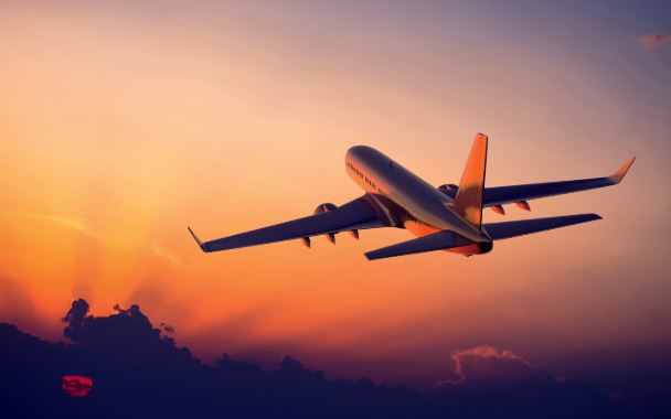 Airplane flying into a colorful sunset sky with clouds.