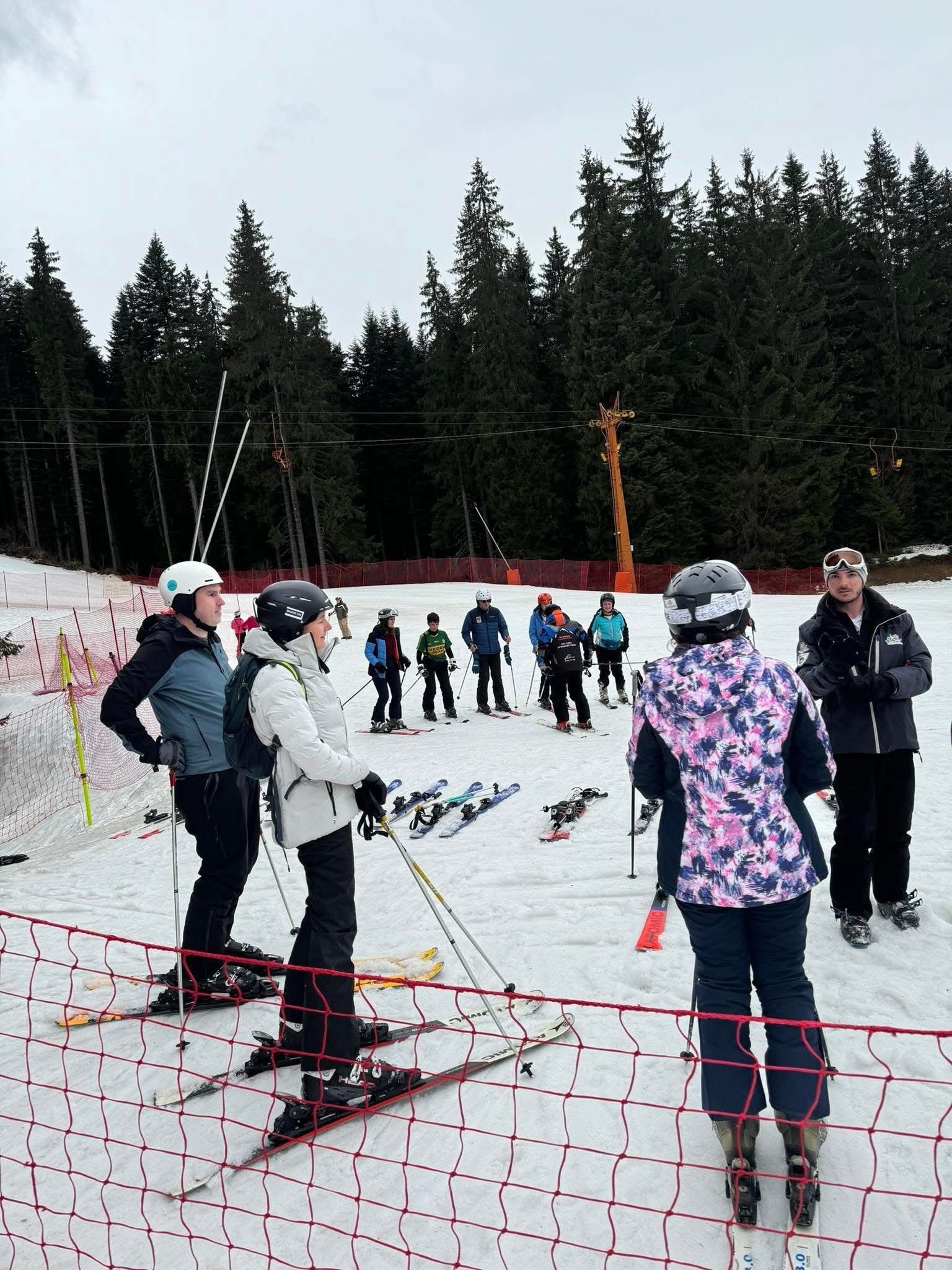 Group of skiers gathered on a snowy slope with trees in the background.