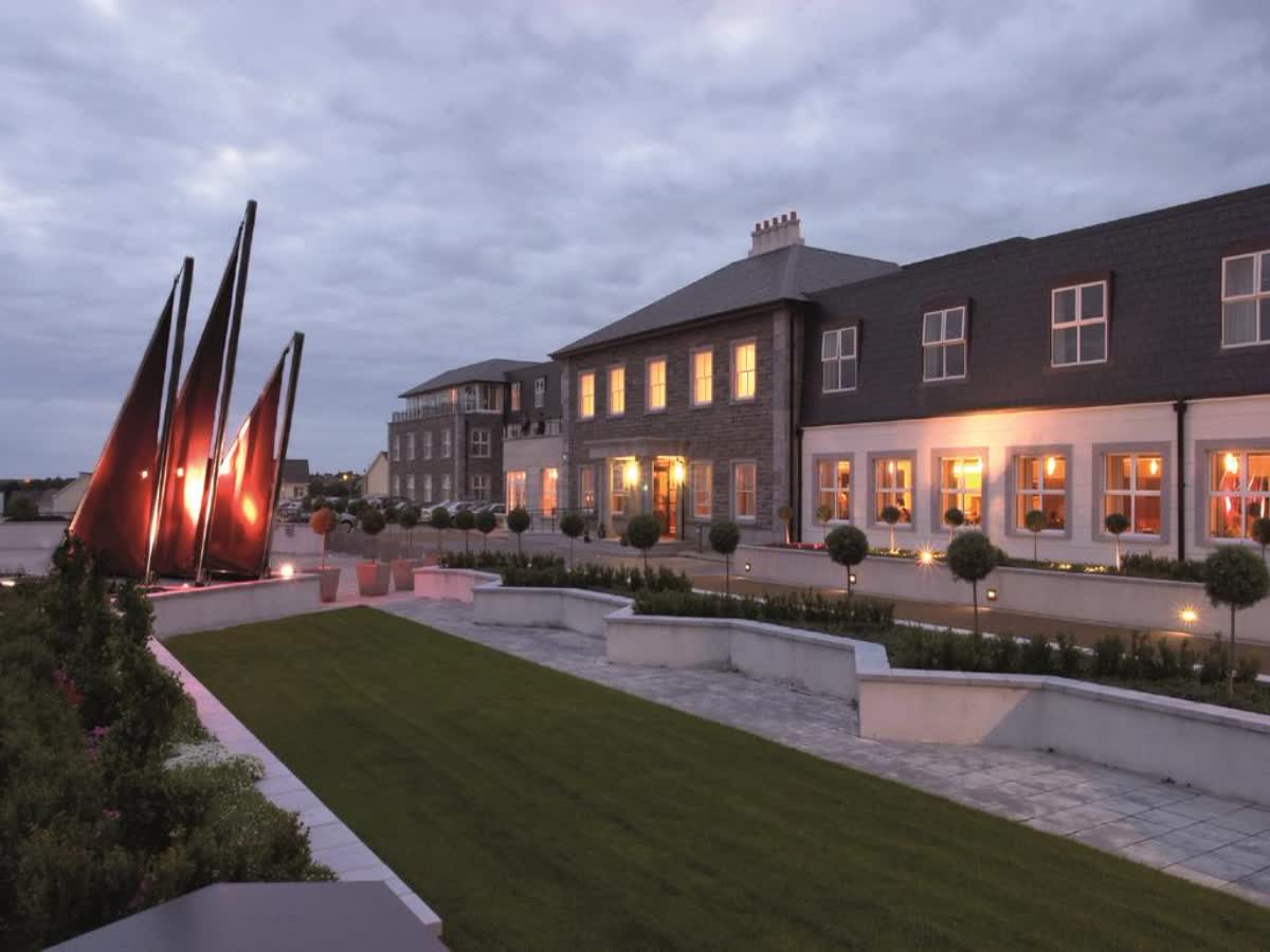 Modern building with illuminated sculpture and landscaped garden at dusk.