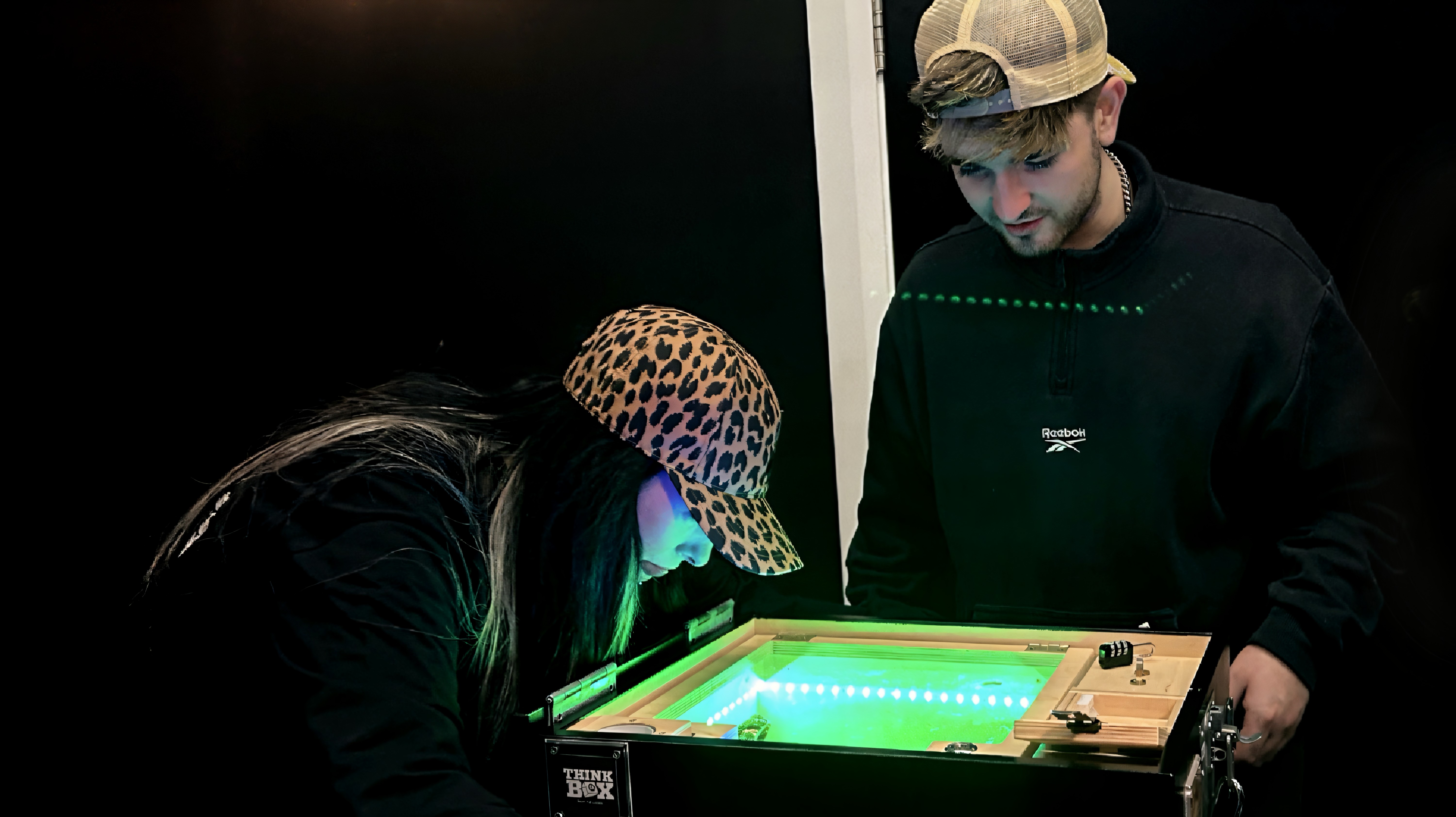 Two people examining a glowing green box with lights.