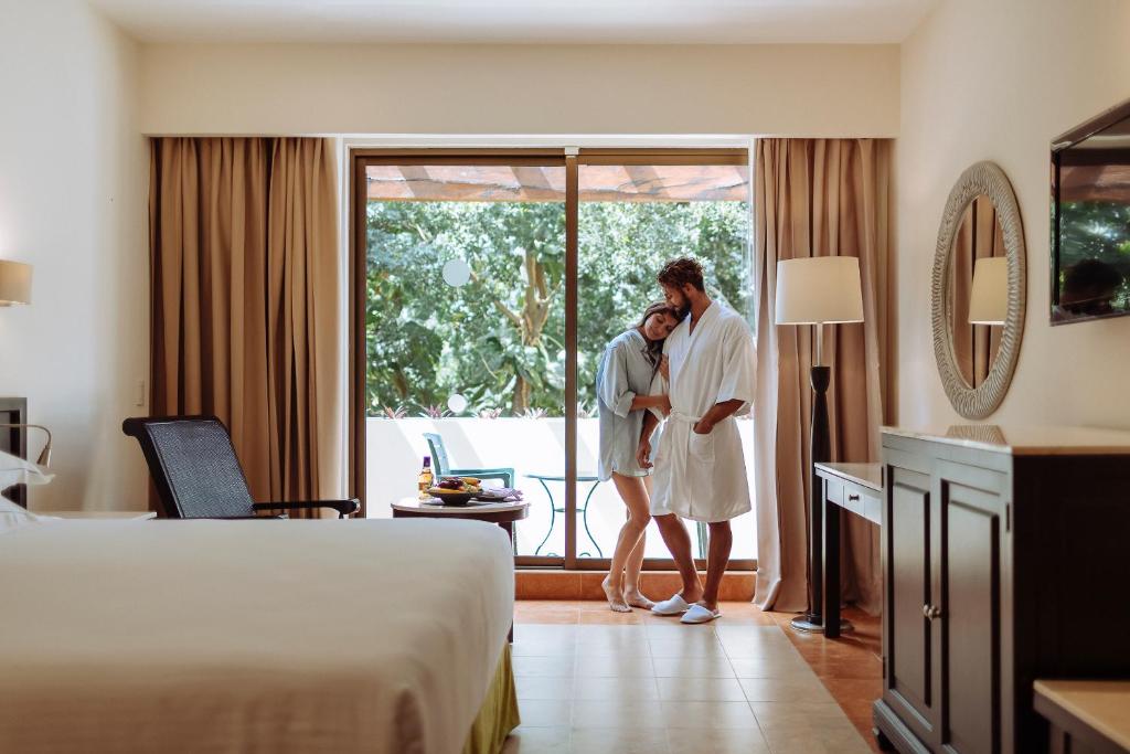 Couple in robes standing by a window in a hotel room.