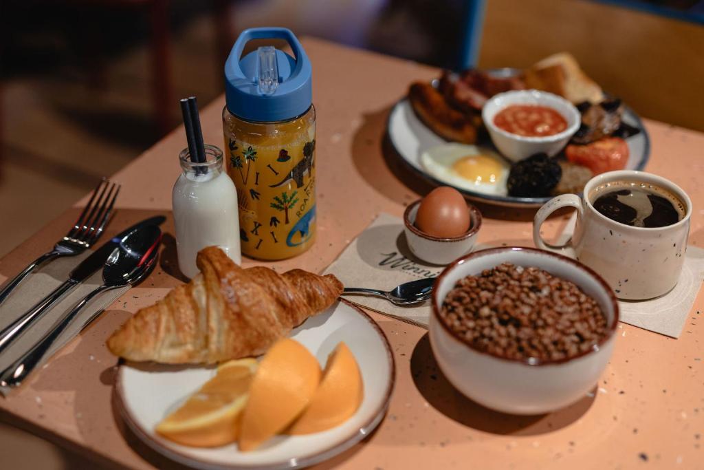 A large breakfast spread on a table, including a full English breakfast, a croissant, cereal, and coffee.
