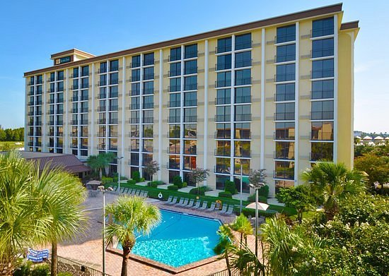 Tall hotel building with a pool and palm trees in front.