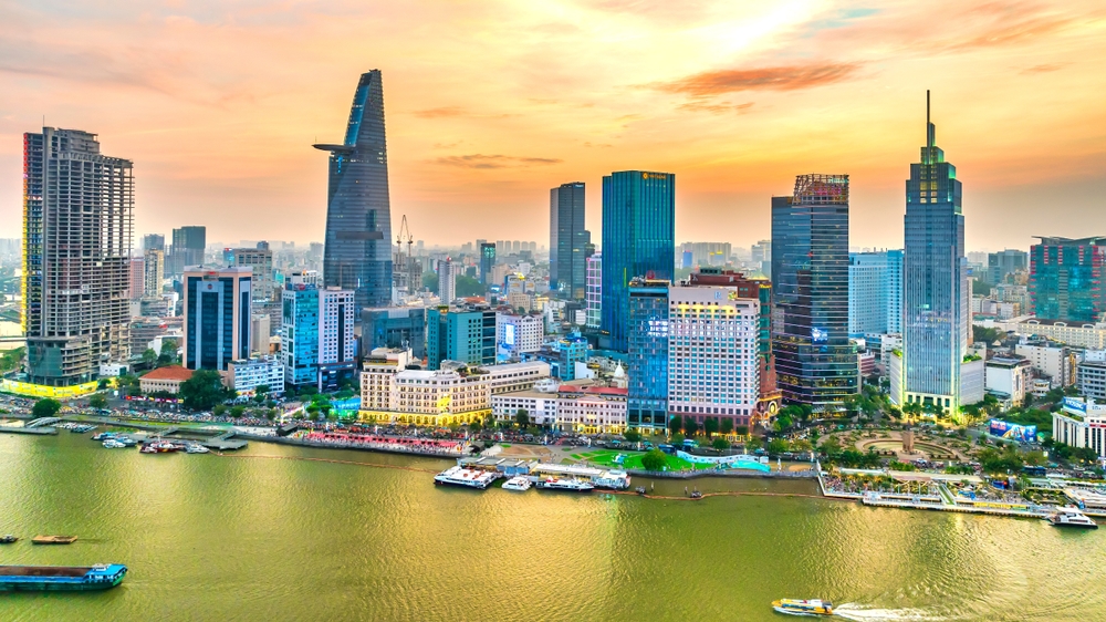 An aerial view of the Ho Chi Minh City skyline with skyscrapers along the Saigon River at sunset.