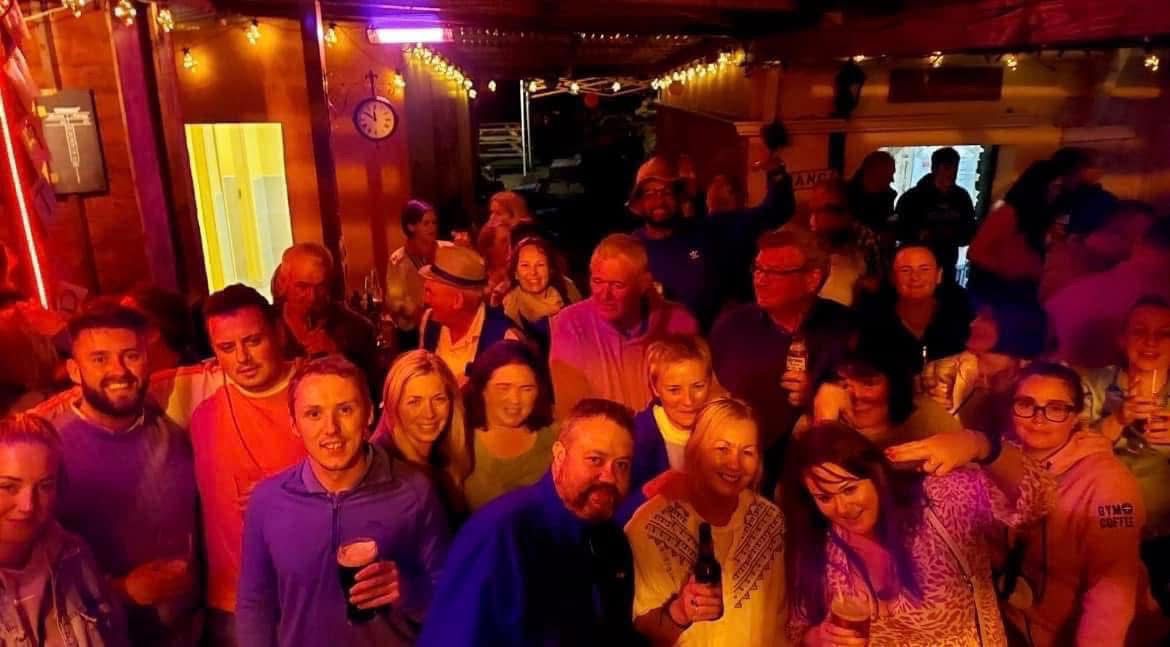A group of people smiling and holding drinks at a lively indoor gathering.