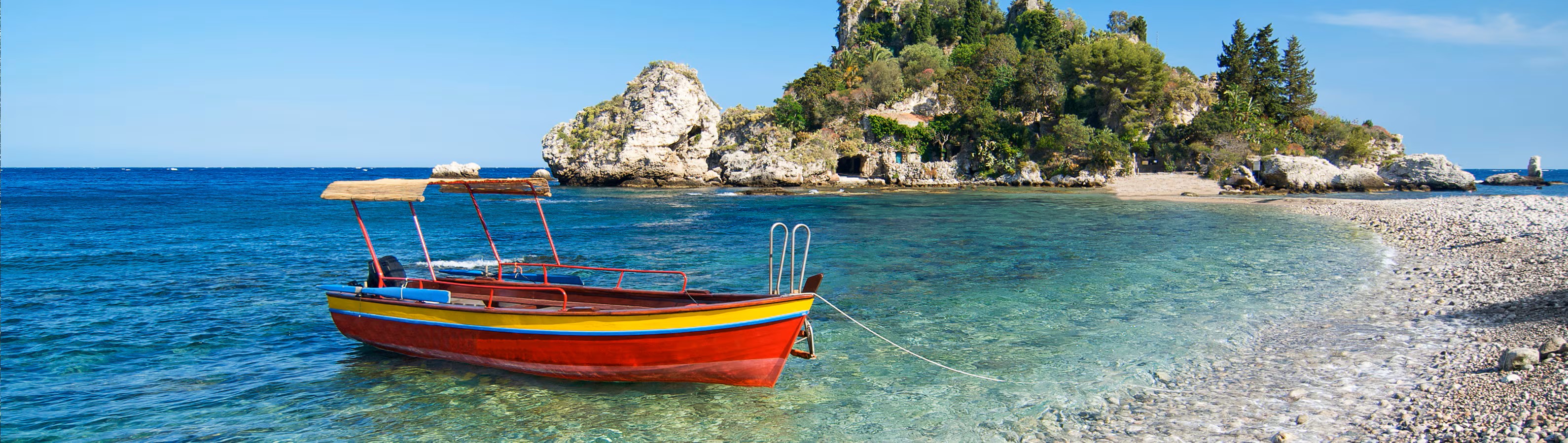 Colorful boat on clear water near a rocky, tree-covered island.