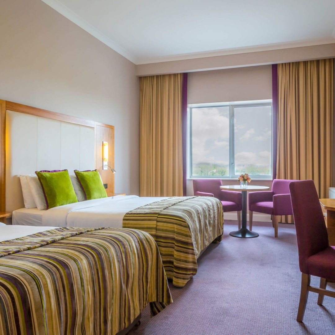 Hotel room with two beds, green pillows, and a window view.